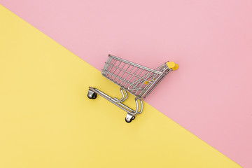 Metal shopping cart on pink and yellow backgrounds.