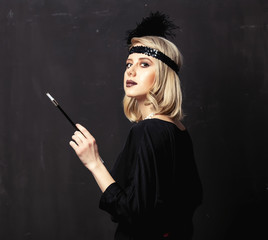Beautiful blonde woman in twenties years clothes with smoking pipe on dark background