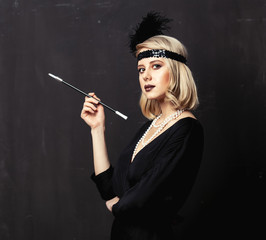 Beautiful blonde woman in twenties years clothes with smoking pipe on dark background