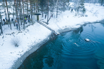 Aerial view of people bathing in an icy and cold blue lake with snow in the winter in the mountains...