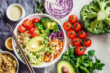 Buddha bowl salad with quinoa, avocado, broccoli, sweet potato and tahini dressing, gray background.