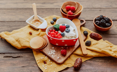 Oats in heart shape bowl with berries on wooden table