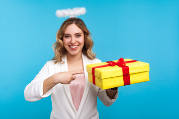 Portrait of happy angelic woman with halo on wavy hair and in white clothes pointing at wrapped...