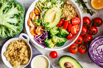 Flat lay of vegan salad with quinoa, avocado, broccoli, sweet potato and tahini dressing, gray background.