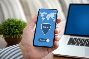 male hand holding phone with app vpn over table laptop