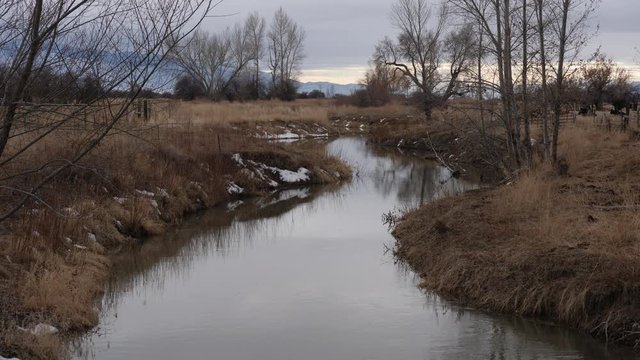 Gentle ripples on slow moving stream under a cloudy winter sky through a pastoral rural countryside