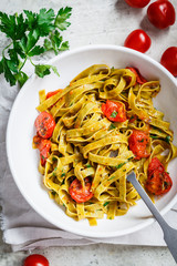 Green spinach pasta with tomatoes and herbs, top view. Healthy vegan food concept.
