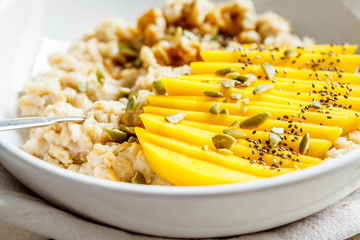 Oatmeal with mango and pumpkin seeds in white bowl. Healthy breakfast, vegan food.