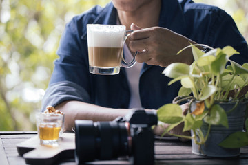 The young man drinks coffee cappuccino in a shady restaurant.