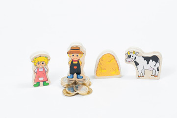 a toy statuette of a man on a large stack of one Euro coins and a statuette of a woman without coins a toy figure of a cow with a haystack on a white background