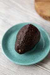 Avocado - dark whole avocado on plate on wooden table. Selective focus
