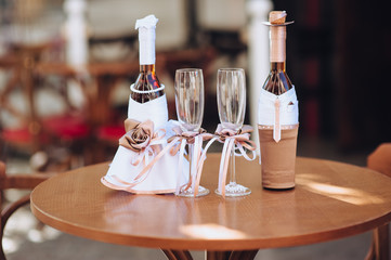 Wedding decorations for the newlyweds. Two decorated bottles, in the form of a bride and groom, glasses with ribbons stand on a wooden table. Photography, concept, composition.