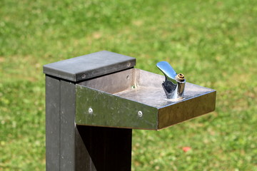 Broken top of dark outdoor public park two level drinking fountain for people and pets surrounded with freshly cut grass