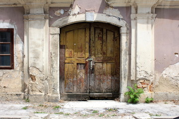 Broken old wooden entrance doors locked with padlock mounted on abandoned suburban family house wall surrounded with decorative frame and cracked concrete in front