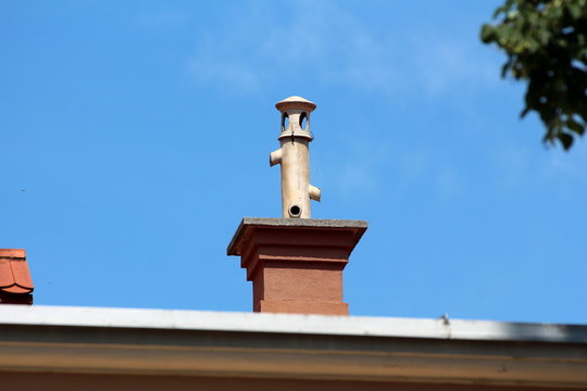 Chimney with unusual pipe on top with multiple openings and protective cap on top of suburban family house roof on clear blue sky background