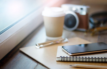 Close-up of mobile phone and notebook put on wooden board with blurred coffee cup and film camera on background
