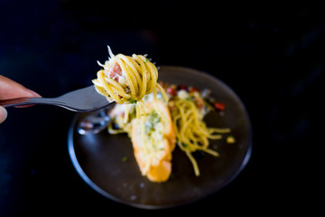 Spaghetti with bacon on a fork, spaghetti with black pepper and bread on black plate. selective focus.