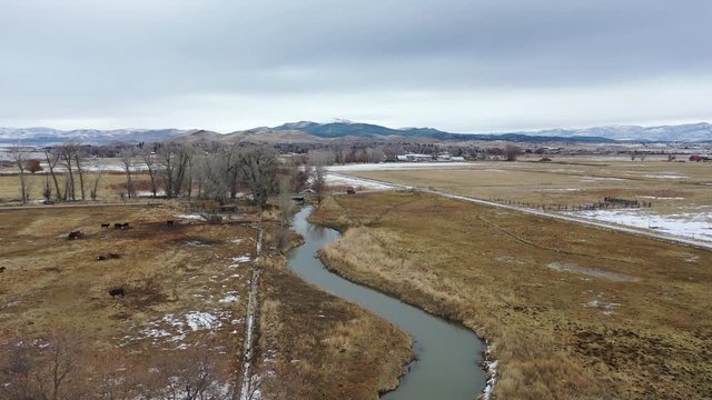 Aerial-Small stream passing through rural pasture land - high fly over on an overcast winter day