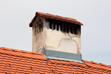 Large old chimney with multiple openings and dilapidated facade surrounded with metal protection and new roof tiles on grey sky background