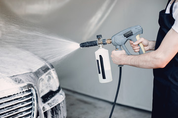 Man in a garage. Worker washing a car. Guy spray a soap