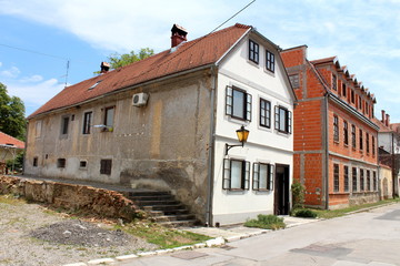 Fototapeta na wymiar Narrow elongated old dilapidated suburban family house with cracked facade and renovated front side next to large newly built red building blocks family house surrounded with paved street in old part 