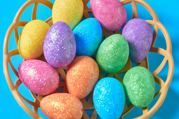 Full plastic basket of colorful eggs with glitters lies on blue table on kitchen. Easter concept. Close-up