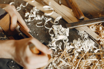 Man working with a wood. Carpenter in a white shirt. Man with a chisel