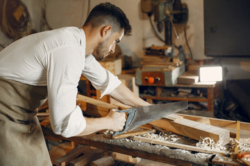Man working with a wood. Carpenter in a white shirt. Worker with a saw