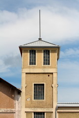 Partially renovated old fire station tower with dilapidated facade and new roof tiles with tall metal pole on top on cloudy blue sky background
