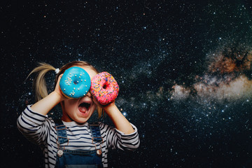 Happy cute girl is having fun played with donuts on cosmos background wall