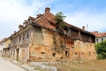 Obraz premium Ruins of large old abandoned suburban family house with destroyed cracked walls and boarded windows in old part of town surrounded with attached houses and paved road
