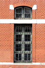 Tall elongated old windows with protective wrought iron bars and decorative frame mounted on red brick wall of local train station
