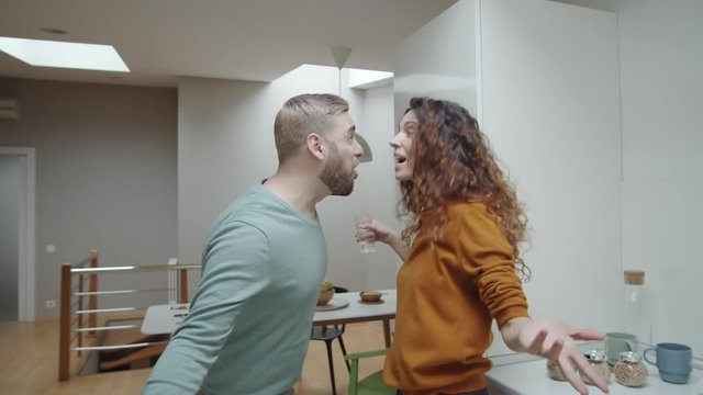 Waist-up shot of emotional young Caucasian boyfriend and girlfriend arguing at home, standing face to face, taunting, abusing and jeering at each other, then woman pushing man away and storming off
