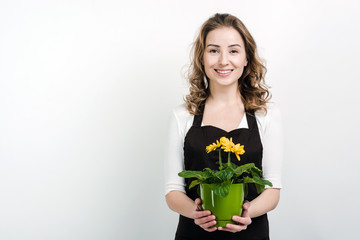 Beautiful, smiling girl holds a flowerpot in her hands, posing in studio on a white wall background