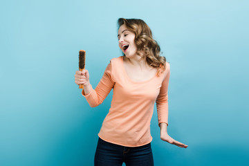 Playful woman sing on a microphone that is actually a hair brush.