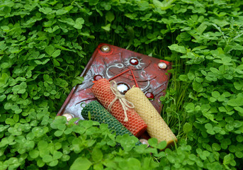 Three colorful wax candles and closed magic book in clover grass.