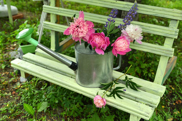 Peony and lupine flowers in watering can on bench in the garden. © samiramay