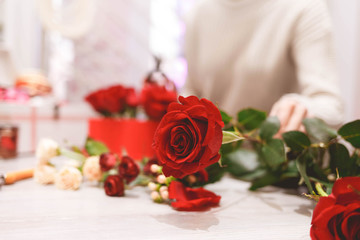 Flower shop florist woman making box with red roses. Process of creating hat-box with flowers