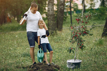 Family on a yard. Father with son planting a tree. Boy with a green funnel