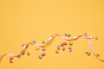 Colored sugar candy jelly beans and silk ribbon bow on a yellow background with copyspace