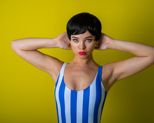 Fototapeta na wymiar Brunette in a striped swimsuit posing in the studio on a bright yellow background. Woman in a short wig with sensual lips.