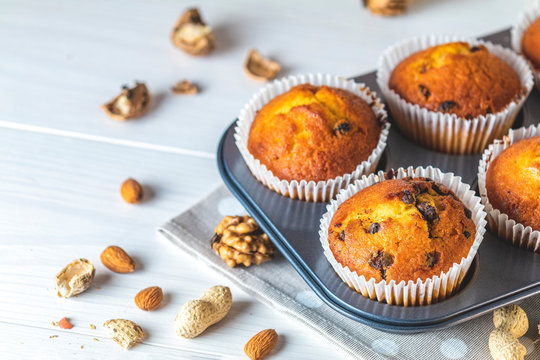 Vanilla caramel muffins in paper cups on white wooden background. Delicious cupcake with raisins, almonds and nuts. Homemade biscuit cakes. Copy space for text..