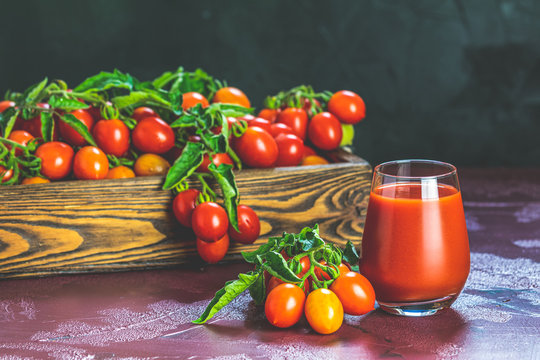 Glass of fresh delicious jummy red tomato juice and fresh tomatoes in wooden box. Dark background. Close up. Gmo free. Natural good food.