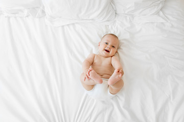 Happy chubby baby lying on white bed holding foot