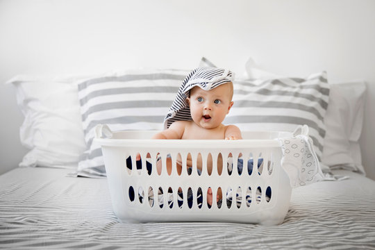 Funny baby sitting in a laundry basket with clothes on top of head