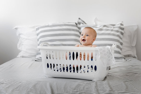 Smiling baby sitting in laundry basket on bed
