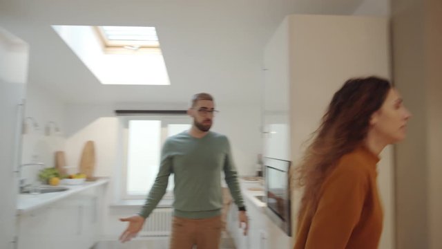 Medium tracking shot of young Caucasian couple arguing at home, woman pushing man, throwing cushions and hitting him on face, then man grabbing her by arms and shaking violently