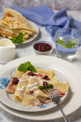 Pancakes on a plate with sour cream and raspberry jam and sprigs of mint with devices on a gray background with a glass of water vertical arrangement
