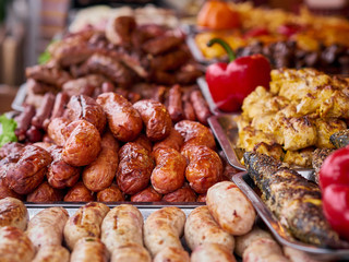 Grilled meat variety at street food store, pork, beef, chicken sausages stacks and red peppers on trays. Unhealthy oily barbeque street fast food for meat lovers concept