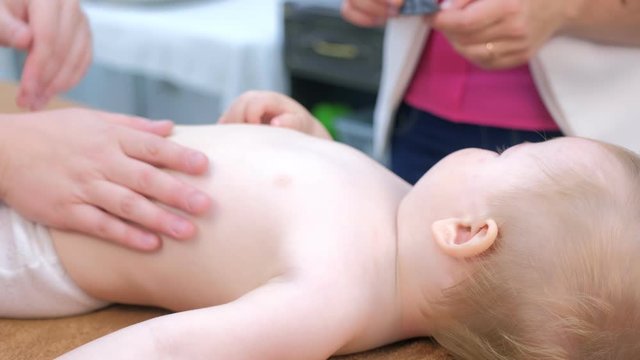 Doctor massagist making massage to baby on tummy in clinic lying on couch. Massagist 's hands gently massaging baby's stomach. Medicine, cure, babycare concept. Hypertonicity problem.